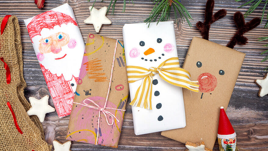 Auf einer rustikalen Holzplatte liegen vier weihnachtlich verpackte und mit Stiften von STAEDTLER bemalte Schokoladentafeln: Ein Nikolaus, ein abstraktes Muster, ein Schneemann und ein Rentier. Foto: Johanna Rundel